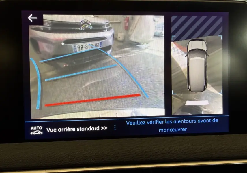 Écran de caméra de recul montrant une voiture grise vue de l’arrière avec lignes de guidage bleues et rouges.