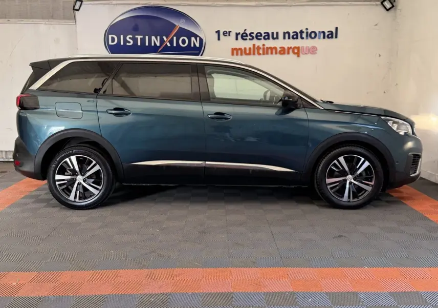Profil droit d’un Peugeot 5008 bleu 2019 avec vitres teintées et jantes alliage bicolores, en intérieur showroom.