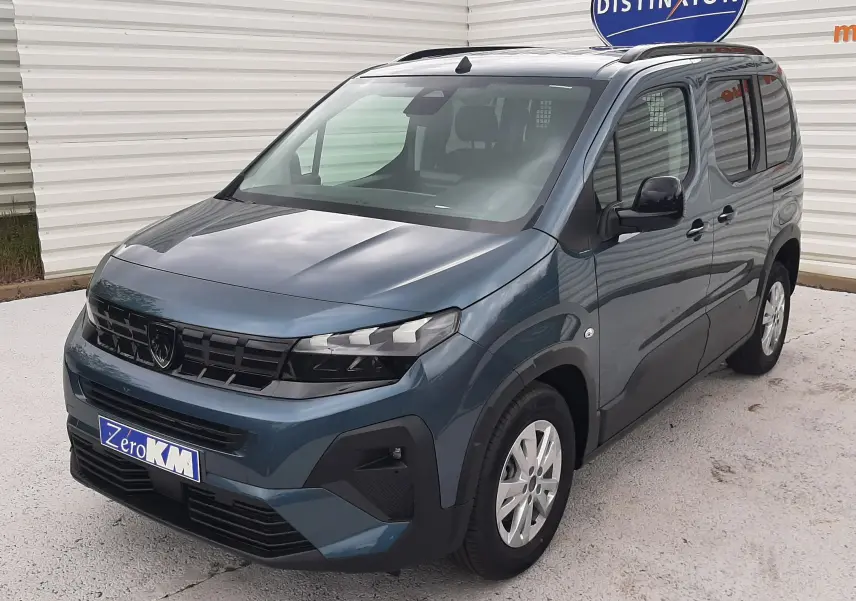 Peugeot Rifter bleu Kiama en 3/4 avant droit, avec calandre noire et jantes argentées, stationné devant un mur blanc.