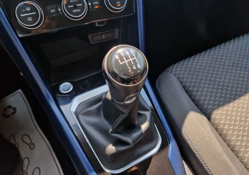 Gros plan sur le levier de vitesses manuel du Volkswagen T-Roc 1.0 TSI 115 United, intérieur avec sellerie noire et console bleue.