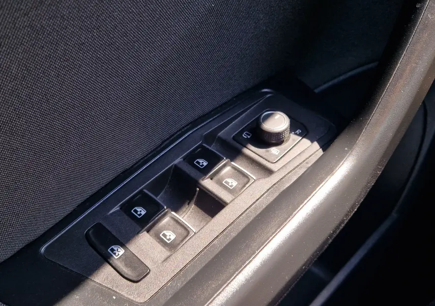 Gros plan sur les commandes des vitres électriques et réglage des rétroviseurs côté conducteur du Volkswagen T-Roc gris foncé.