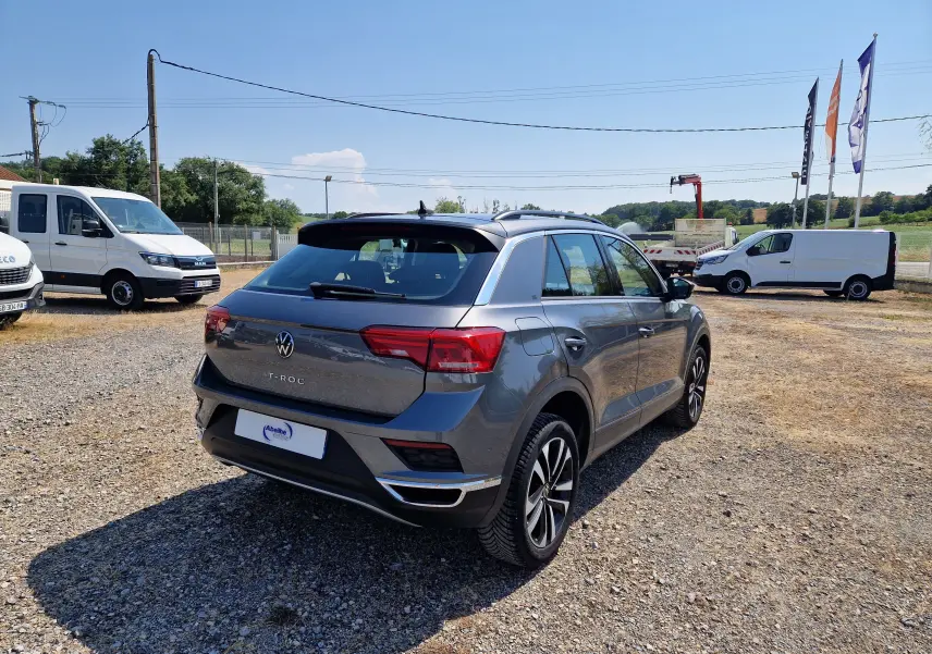 Volkswagen T-Roc gris foncé métal vu en 3/4 arrière droit sur un terrain extérieur ensoleillé.