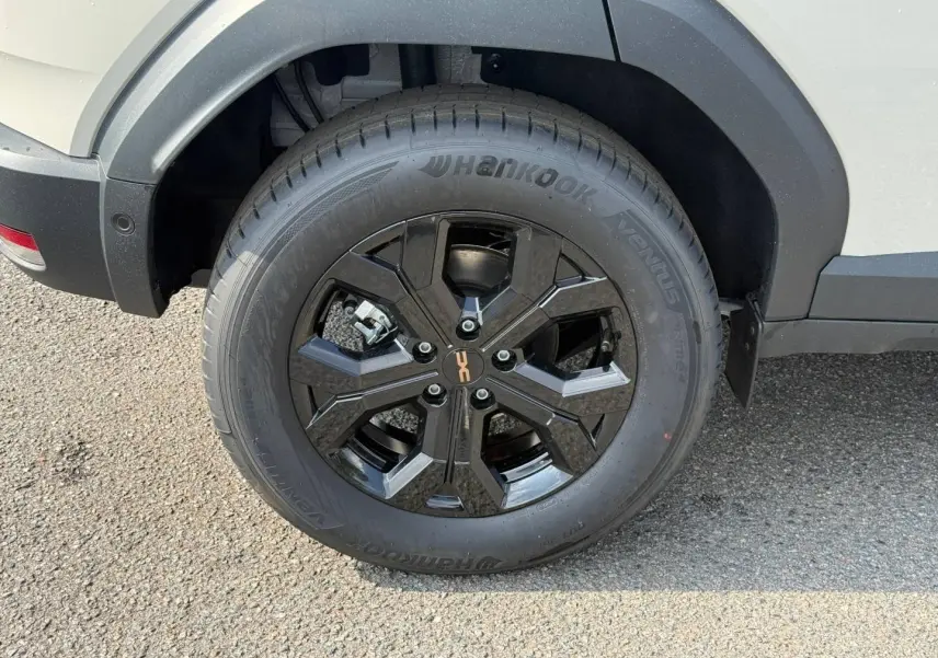 Gros plan sur la roue arrière droite du Dacia Duster blanc 2026 avec jante alu noire et logo central orange.