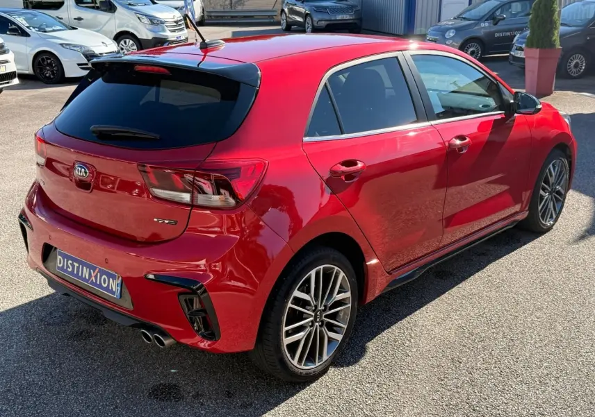 Vue 3/4 arrière droite d'une KIA RIO GT-LINE rouge grenadine avec jantes alliage et double sortie d'échappement chromée.
