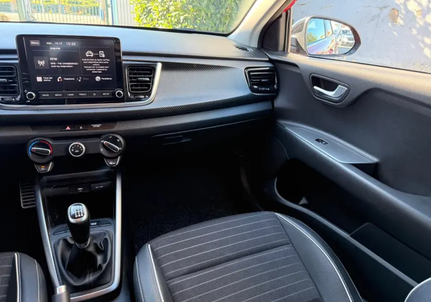 Intérieur côté passager de la Kia Rio 2022, montrant la console centrale avec boîte manuelle et tableau de bord noir.
