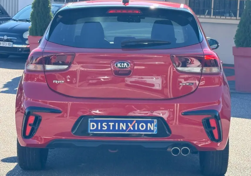 Vue arrière d'une KIA RIO rouge grenadine 2022 avec double sortie d'échappement et plaque Distinxion visible.