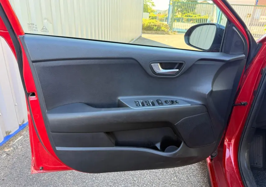Porte avant gauche ouverte d'une KIA Rio rouge grenadine 2022, montrant les commandes électriques et le haut-parleur intégré.