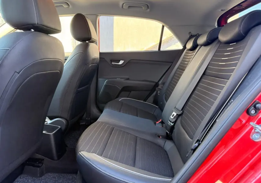 Vue intérieure côté gauche des sièges arrière noirs avec surpiqûres blanches d'une KIA RIO rouge grenadine 2022.