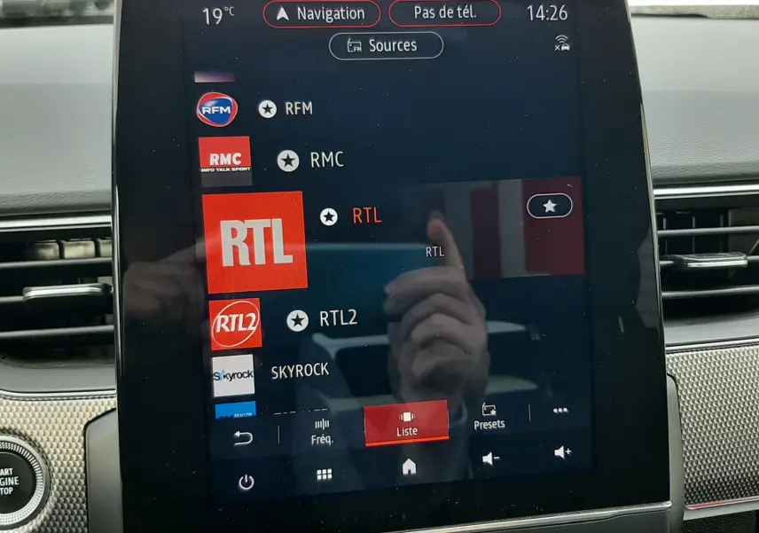 Écran tactile central du tableau de bord du Renault Arkana rouge Flame 2021 affichant les stations radio avec interface moderne.
