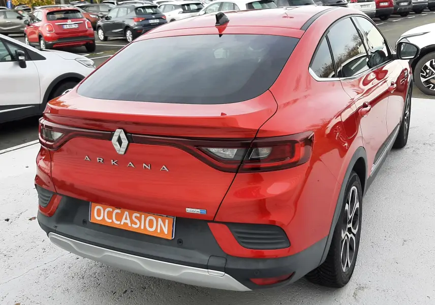Vue 3/4 arrière droite d'un Renault Arkana rouge flamme avec feux LED et plaque "OCCASION" sur parking.