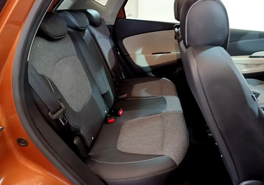 Vue intérieure du côté arrière gauche du Renault Captur Intens orange, montrant la banquette arrière en tissu gris et noir.