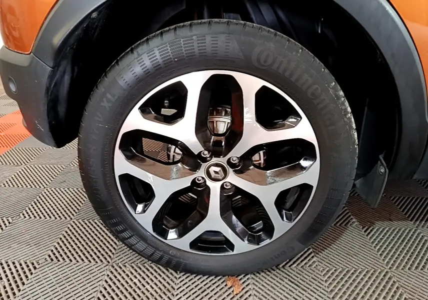 Gros plan sur la roue avant gauche du Renault Captur orange, mettant en valeur la jante alliage bicolore et le logo Renault central.