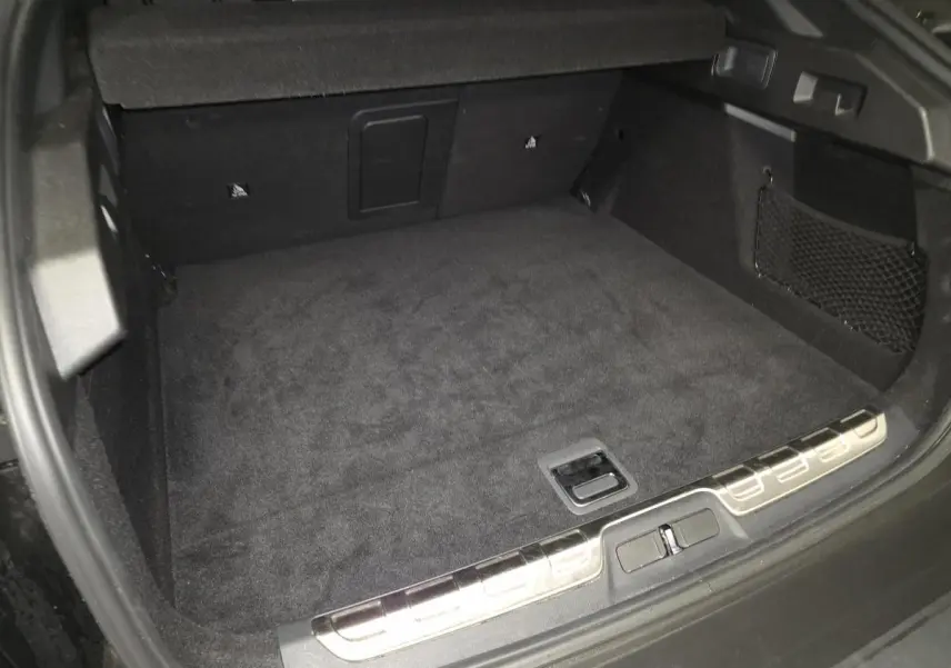 Coffre ouvert vu de l'arrière d'une Peugeot 408 noire, avec tapis de sol noir et filet de rangement latéral.