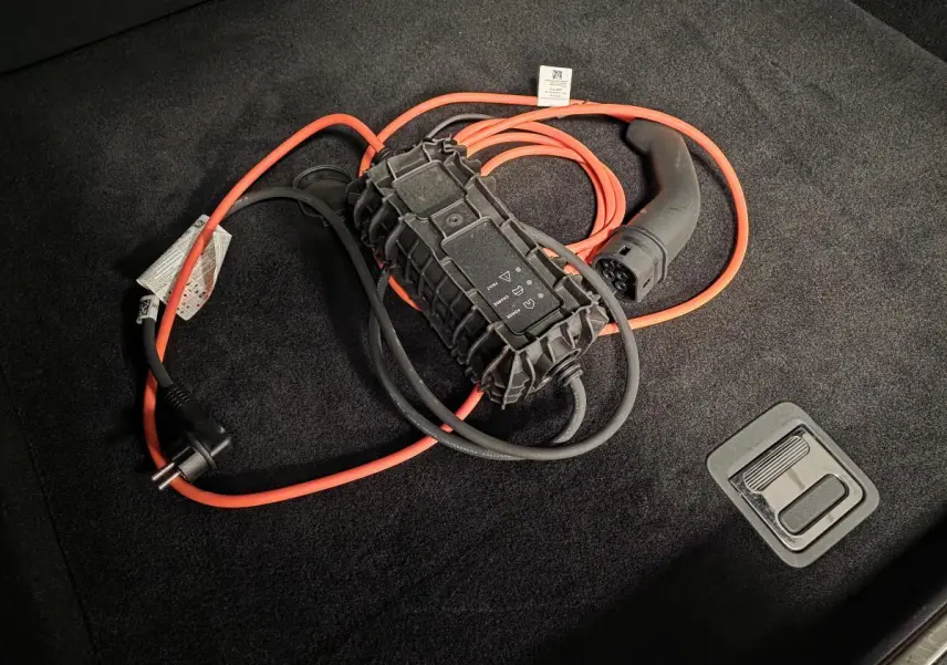 Câble de recharge orange et noir posé sur le tapis noir du coffre d'une Peugeot 408 hybride rechargeable 2024.