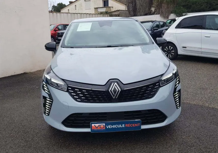 Vue avant d'une Renault Clio gris clair 2025 avec calandre noire et feux LED verticaux allumés.