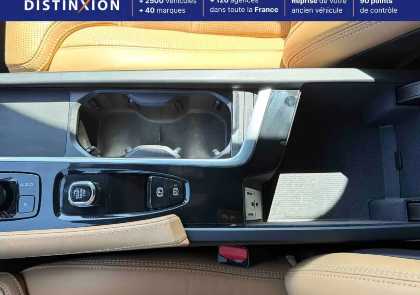 Vue plongeante sur la console centrale cuir beige du Volvo XC90 gris avec bouton démarrage et porte-gobelets.