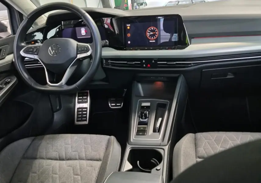 Vue intérieure avant de la Volkswagen Golf 8 avec tableau de bord numérique, volant multifonction et sellerie tissu gris.