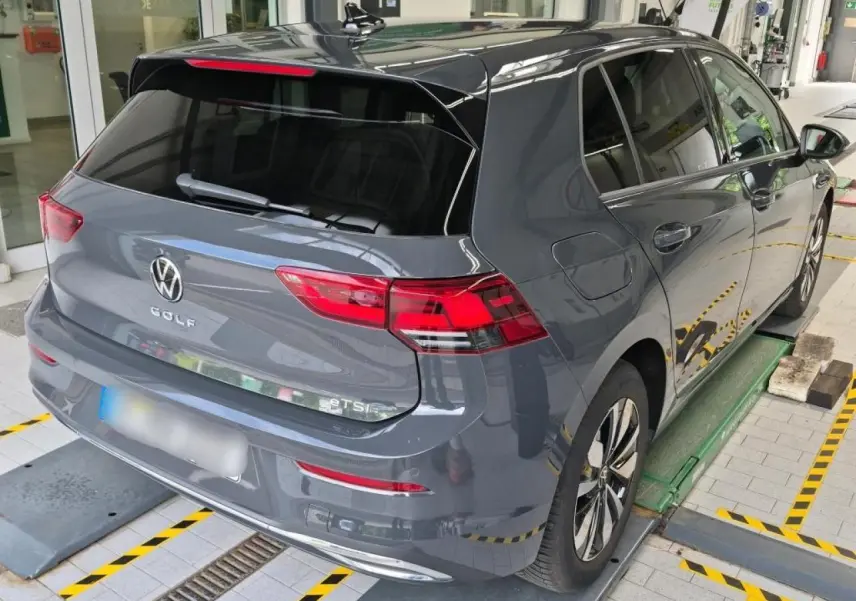 Vue 3/4 arrière droite d'une Volkswagen Golf 8 gris Urano avec feux arrière LED et vitres teintées.