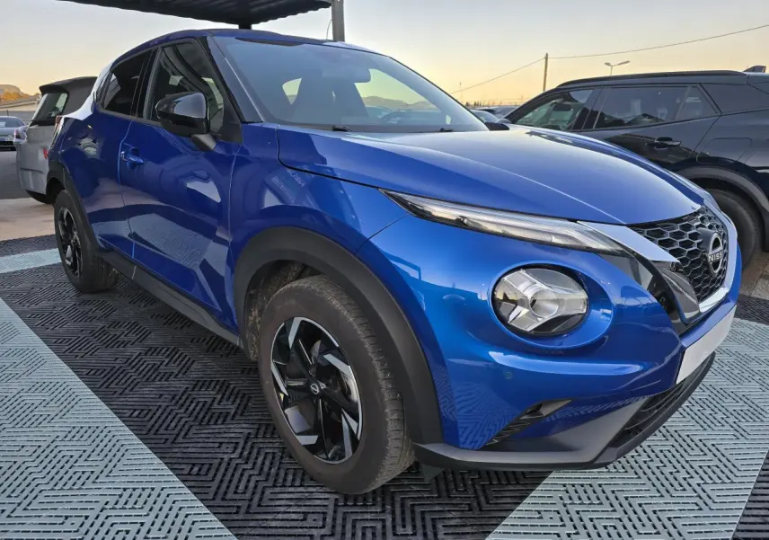 Nissan Juke II bleu magnetic en vue 3/4 avant droit, avec jantes alliage noires et calandre V-Motion distinctive.