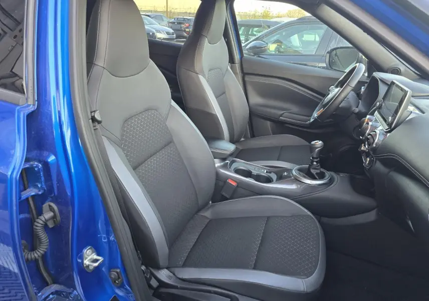Intérieur avant droit du Nissan Juke II bleu magnetic 2024, sièges TEP/tissu noirs et console centrale avec boîte manuelle.
