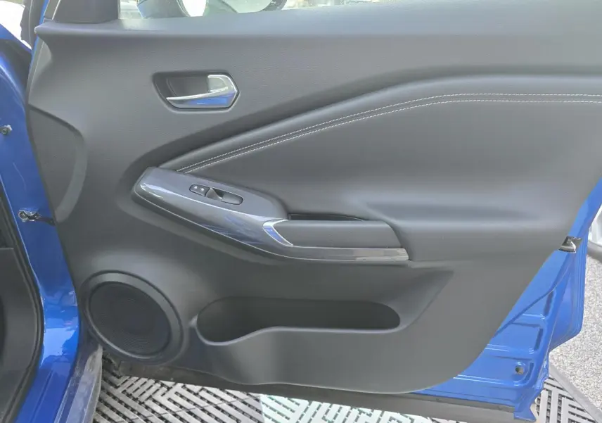 Détail de la porte avant gauche bleu magnetic du Nissan Juke II avec commande de lève-vitre et haut-parleur intégré.
