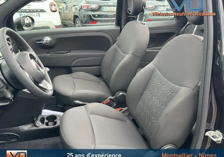 Vue intérieure côté conducteur de la FIAT 500C noire 2024, sièges avant en tissu gris et volant visible.