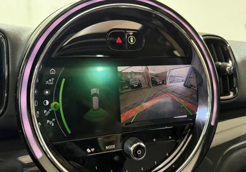 Gros plan sur l'écran tactile rond du tableau de bord du MINI Countryman noir, affichant la caméra de recul et l'aide au stationnement.