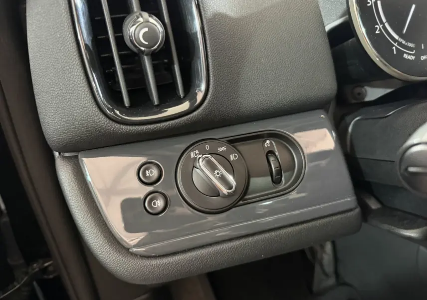 Gros plan sur les commandes d'éclairage gris brillant à gauche du volant dans l'habitacle noir du MINI COUNTRYMAN 2020.