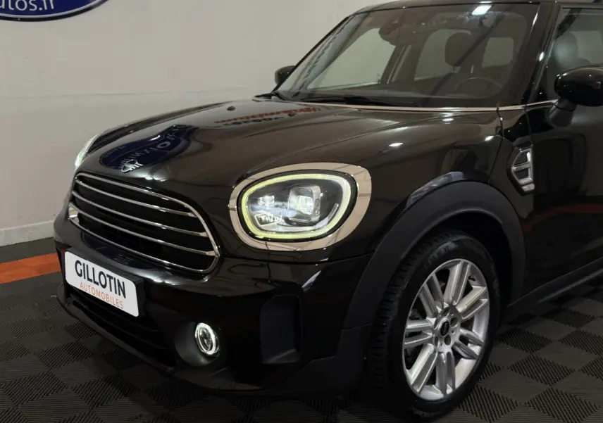 Vue 3/4 avant d'une MINI Countryman noire avec phares LED et jantes alliage argentées visibles en intérieur showroom.