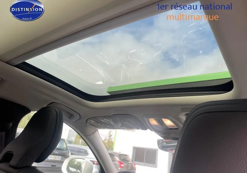 Vue intérieure du toit panoramique en verre du Volvo XC60 gris, avec sièges avant en cuir noir et éclairage intérieur allumé.