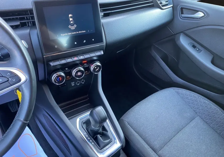 Intérieur de Renault Clio V E-Tech blanc, vue côté passager sur console centrale avec écran tactile et levier de boîte auto.
