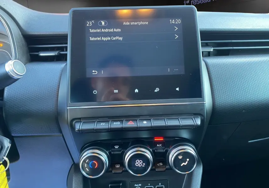 Tableau de bord de Renault Clio V blanc, vue frontale centrée sur l'écran tactile et les commandes de climatisation.