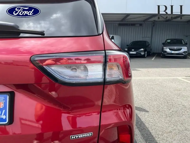 Gros plan sur l'arrière droit du Ford Kuga rouge Premium Lucid avec feu arrière et badge Hybrid visibles.