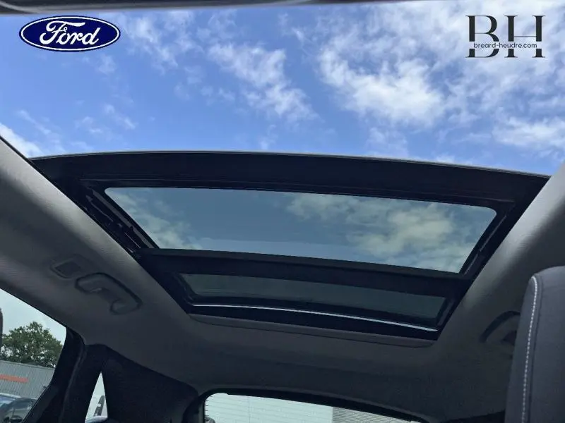 Toit panoramique ouvert vu de l'intérieur du Ford Kuga 2022, laissant apparaître un ciel partiellement nuageux.