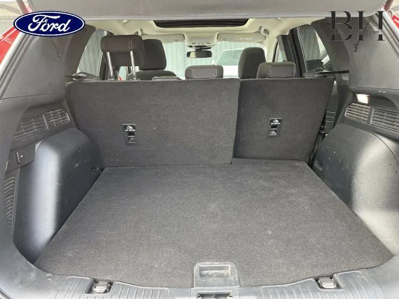 Coffre spacieux du Ford Kuga 2022 en Premium Rouge Lucid, vue intérieure arrière avec banquette arrière partiellement relevée.