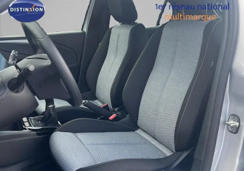 Vue intérieure côté conducteur de l'Opel Corsa gris 2025, montrant les sièges avant en tissu bicolore et le volant multifonctions.