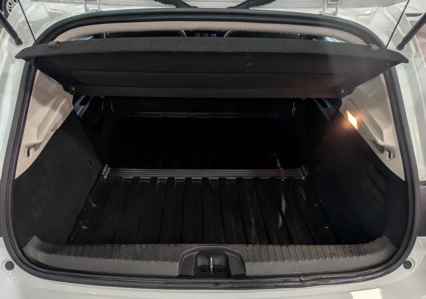 Coffre ouvert vu de l'arrière d'une Renault Clio V Blanc Glacier, avec cache-bagages et éclairage intérieur allumé.