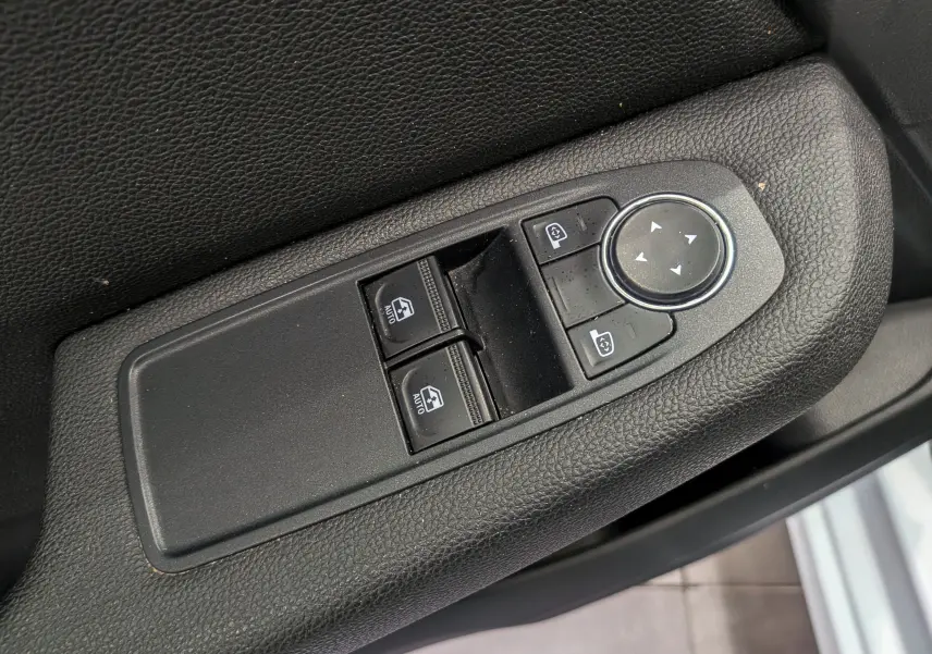 Gros plan sur les commandes de lève-vitres et réglage des rétroviseurs côté conducteur d'une Renault Clio V blanche.