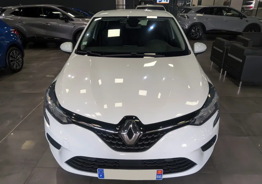 Vue avant d'une Renault Clio V blanche Glacier en showroom, mettant en valeur la calandre noire et le logo Renault central.