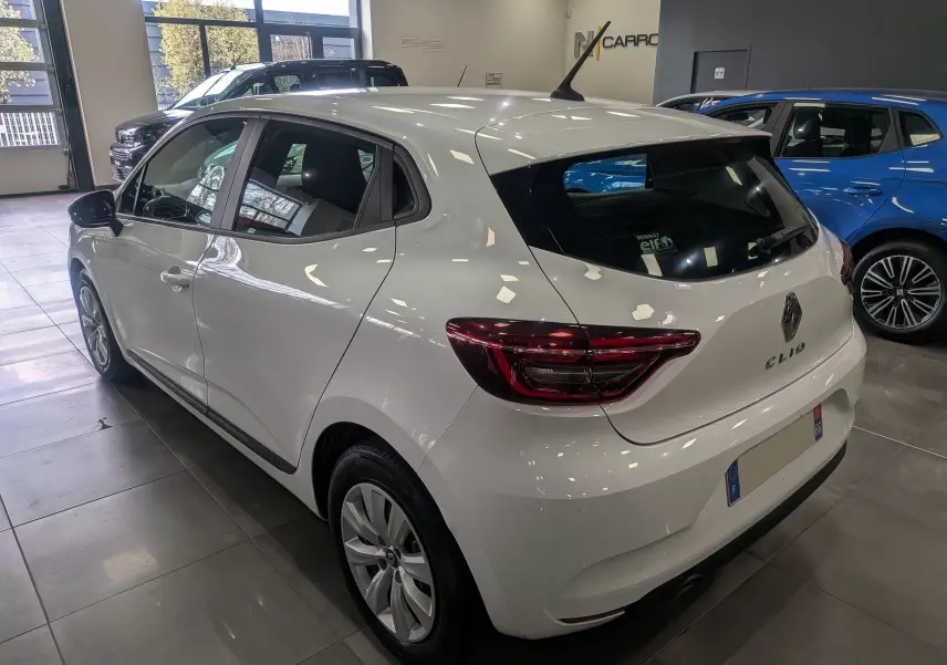Vue 3/4 arrière droite d'une Renault Clio V blanche Glacier en showroom, avec feux arrière LED et antenne requin.