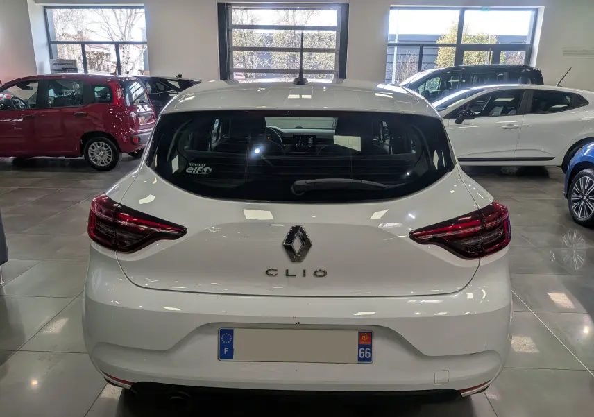 Vue arrière d'une Renault Clio V blanche Glacier, version Société, dans un showroom avec d'autres véhicules visibles.