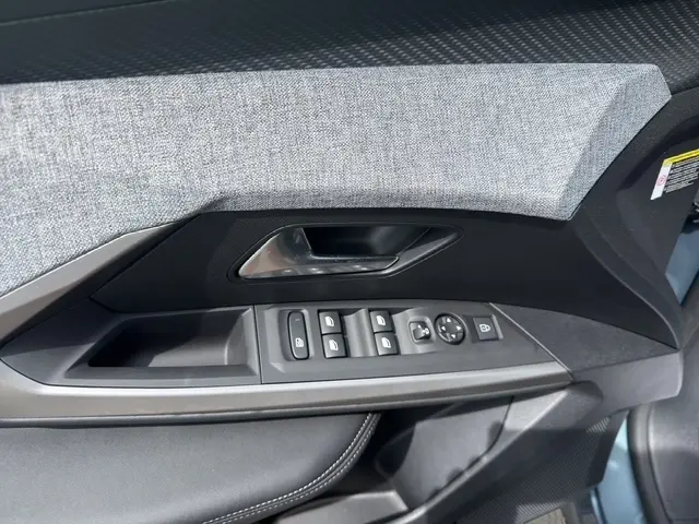 Détail de la porte côté conducteur du Peugeot 3008 bleu 2025, avec commandes électriques et habillage tissu gris.