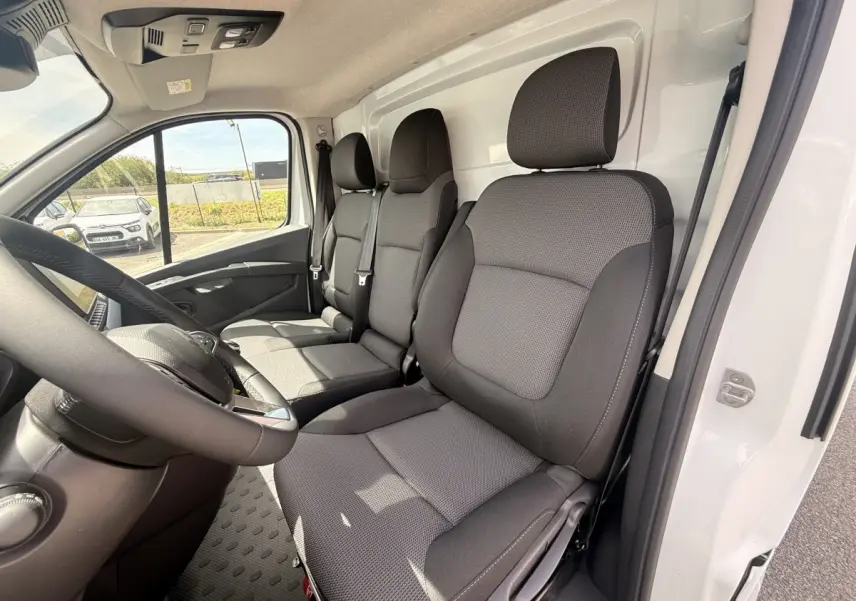 Vue intérieure côté conducteur du Renault Trafic Fourgon blanc 2025, montrant les sièges avant en tissu gris.