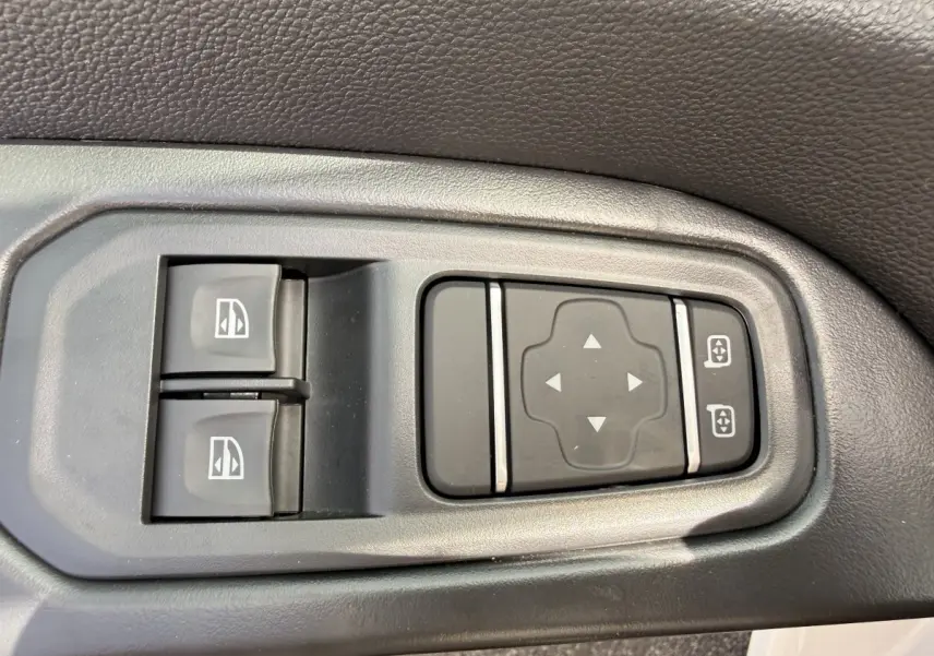 Gros plan sur les commandes électriques des vitres et rétroviseurs côté conducteur du Renault Trafic Fourgon blanc.