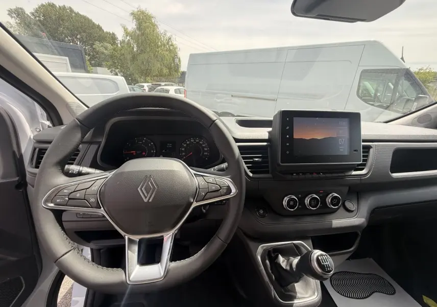 Vue intérieure du tableau de bord et volant multifonctions du Renault Trafic Fourgon blanc, avec écran tactile central et boîte manuelle.