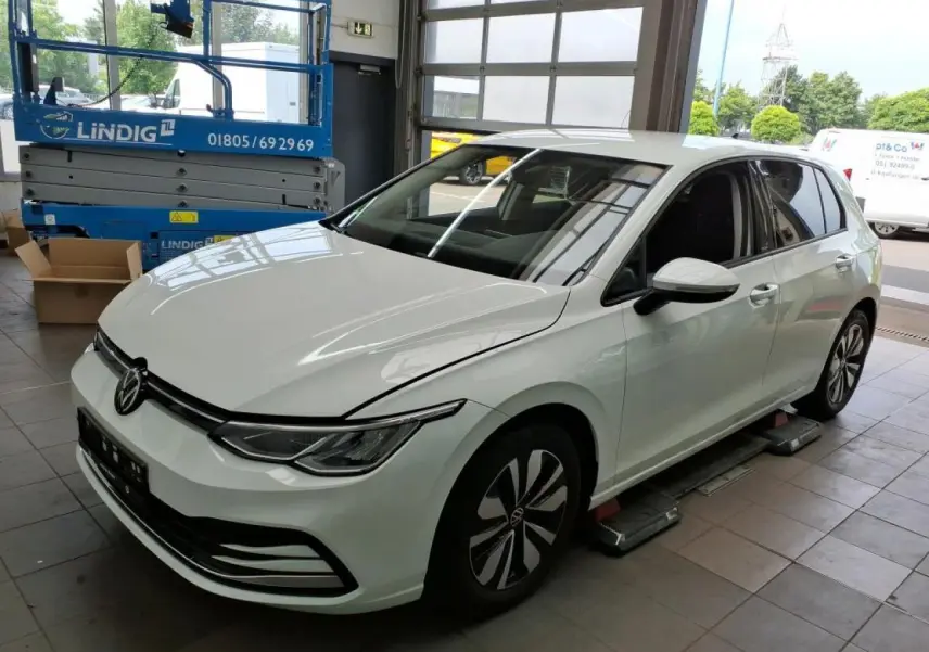 Volkswagen Golf 8 blanche vue 3/4 avant droit en intérieur avec jantes distinctives et phares LED.