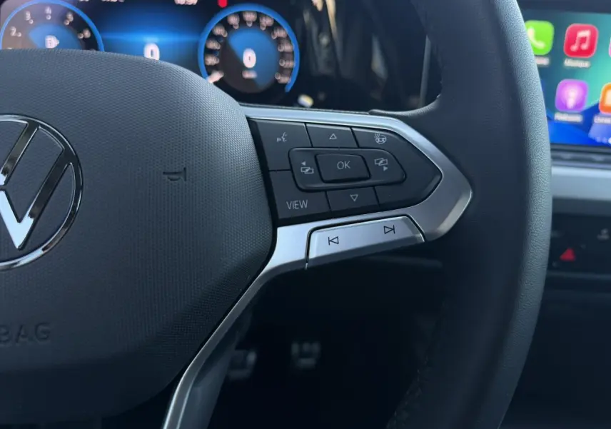 Gros plan sur le volant multifonction noir de la Volkswagen Golf 8 avec commandes intégrées et tableau de bord numérique en arrière-plan.