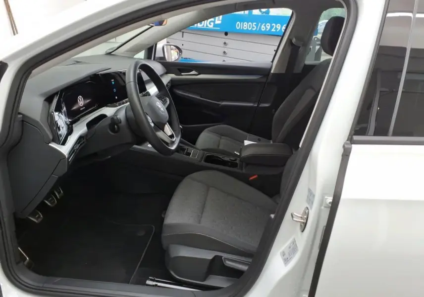 Intérieur de la Volkswagen Golf 8 blanche, vue côté conducteur avec tableau de bord digital et sièges tissu gris.
