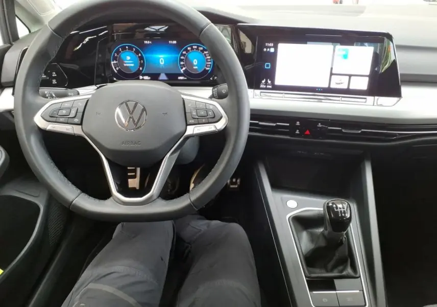 Vue intérieure centrée sur le volant multifonction et la console avec levier de vitesse manuelle d'une Volkswagen Golf 8 blanche.