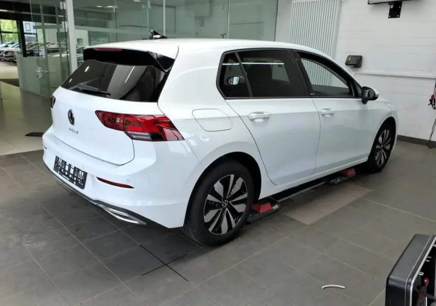 Volkswagen Golf 8 blanche vue 3/4 arrière droit en intérieur avec jantes alliage et vitres teintées.